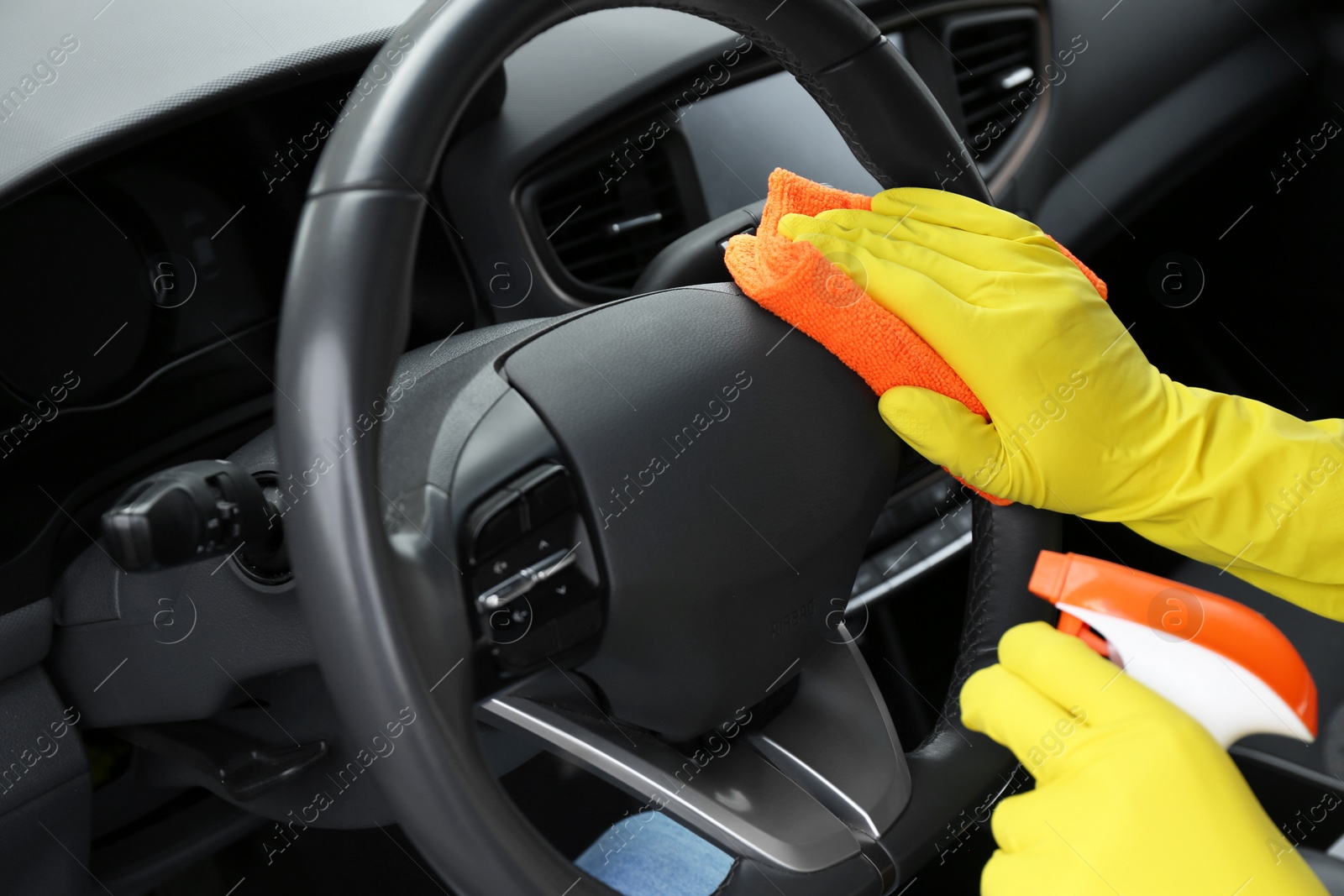 Photo of Woman cleaning steering wheel with rag in car, closeup