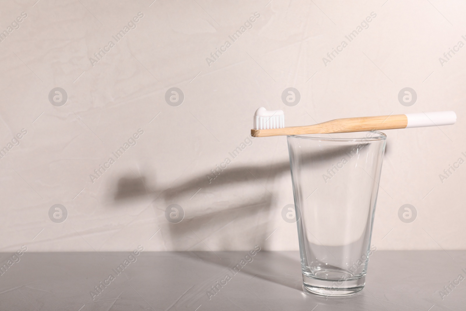 Photo of Glass with bamboo toothbrush on table against grey background. Space for text