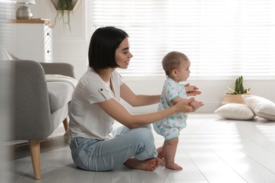 Photo of Mother supporting her baby daughter while she learning to walk at home