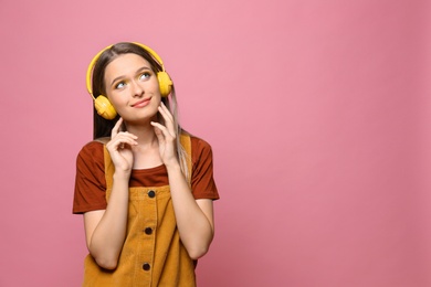 Photo of Happy teenage girl with headphones on pink background. Space for text