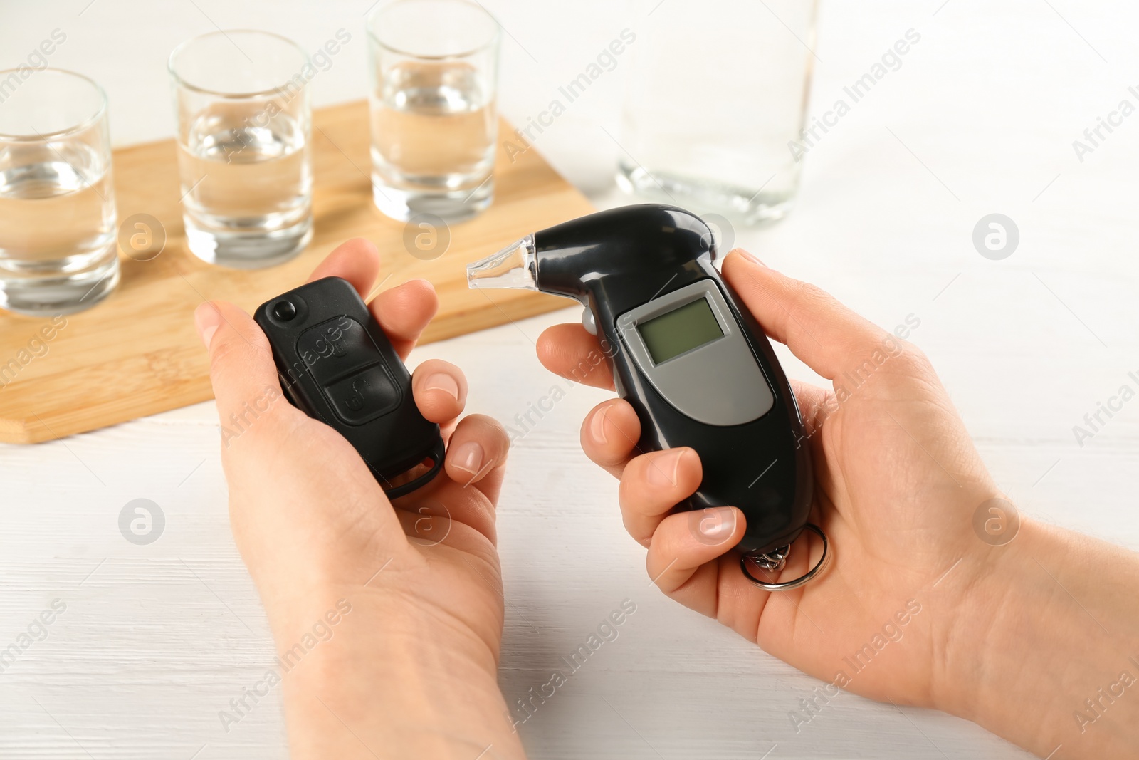 Photo of Woman holding modern breathalyzer and car key near white table with alcohol, closeup