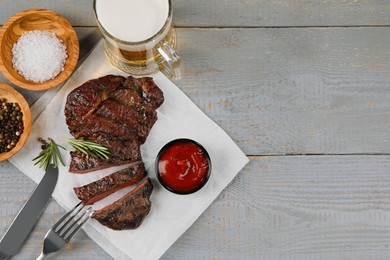 Photo of Mug with beer, fried steak and sauce on grey wooden table, flat lay. Space for text