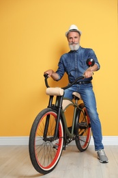 Photo of Portrait of handsome mature man with bicycle near color wall