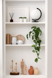 Stylish shelves with decorative elements and houseplant near white wall. Interior design