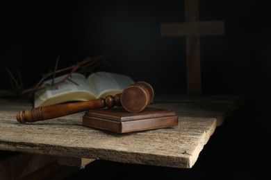 Photo of Judge gavel, bible, cross and crown of thorns on wooden table against black background