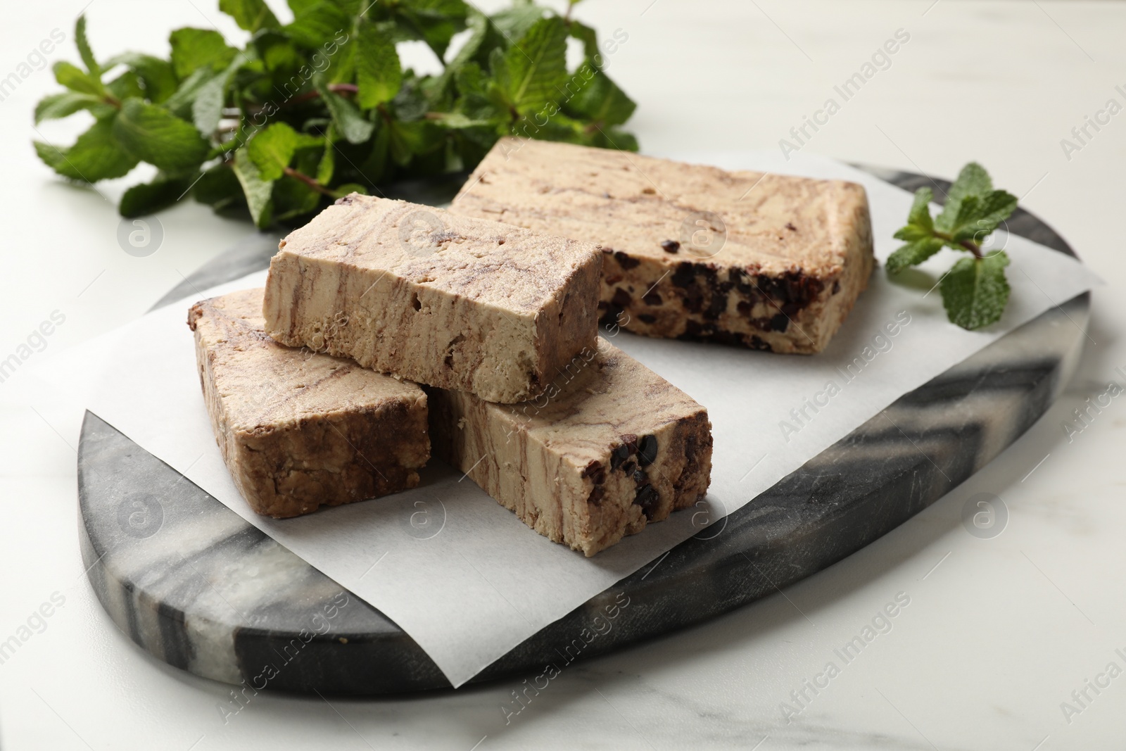 Photo of Pieces of tasty chocolate halva and mint on white marble table, closeup