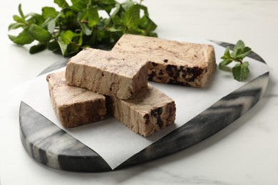 Photo of Pieces of tasty chocolate halva and mint on white marble table, closeup