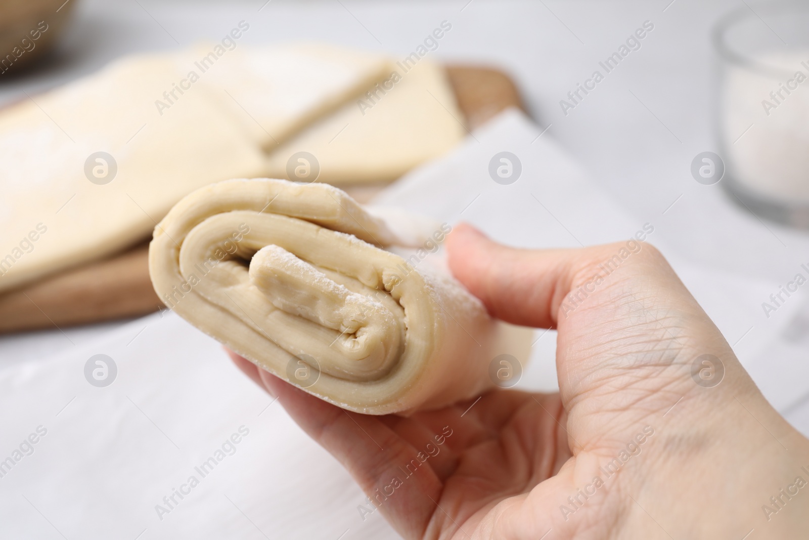 Photo of Woman with raw puff pastry dough at white table, closeup