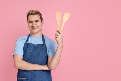 Photo of Portrait of happy confectioner holding wooden spatulas on pink background, space for text