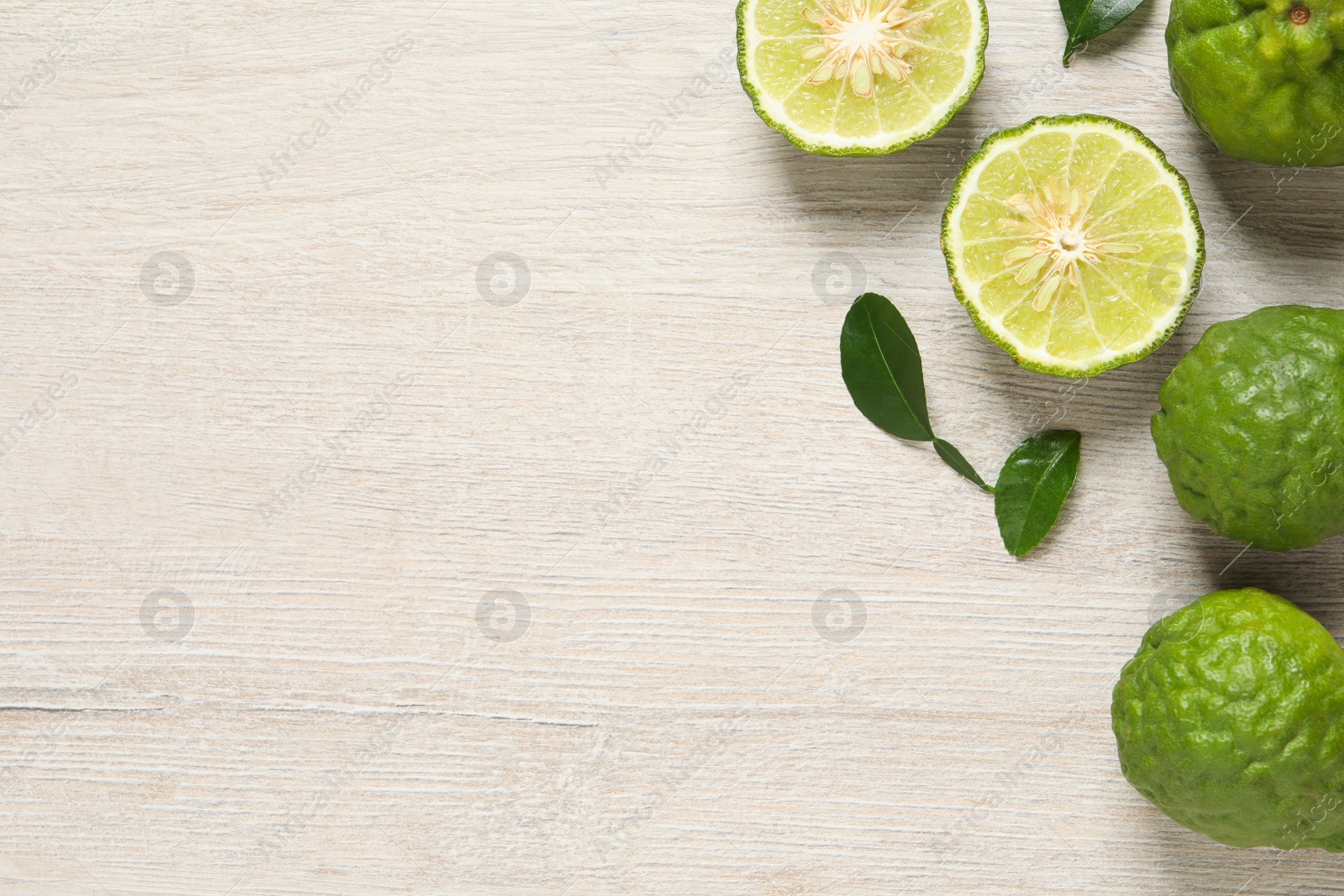 Photo of Whole and cut ripe bergamot fruits with green leaves on white wooden table, flat lay. Space for text