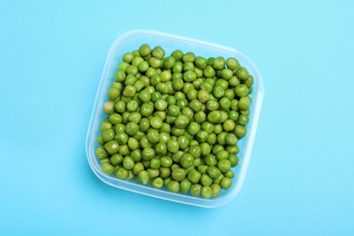 Photo of Fresh peas in glass container on light blue background, top view