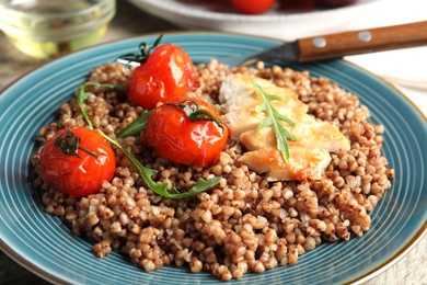 Tasty buckwheat porridge with meat and tomatoes on table, closeup