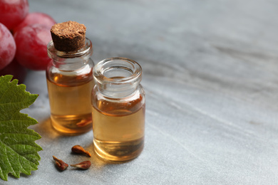 Photo of Bottles of natural grape seed oil on grey table, space for text. Organic cosmetic