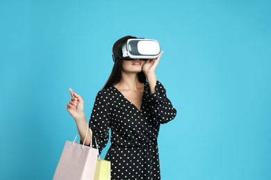 Photo of Woman with shopping bags using virtual reality headset on light blue background