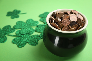 Photo of Pot of gold coins and clover leaves on green background, space for text. St. Patrick's Day celebration