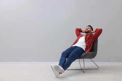 Photo of Handsome man relaxing in armchair near light grey wall indoors, space for text