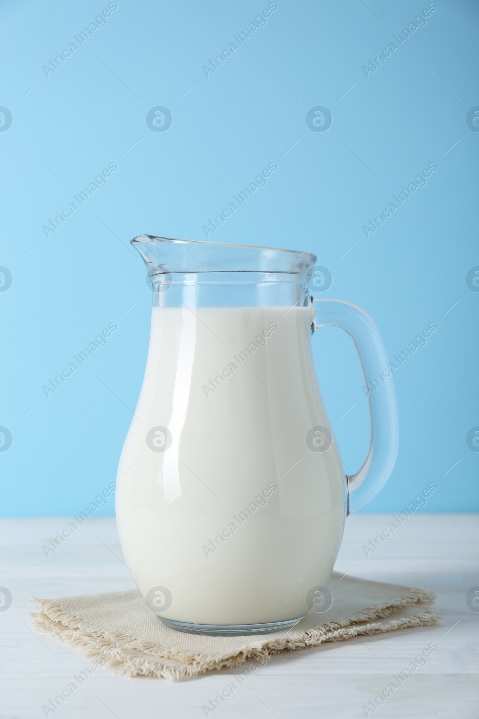 Photo of Jug of fresh milk on white wooden table against light blue background