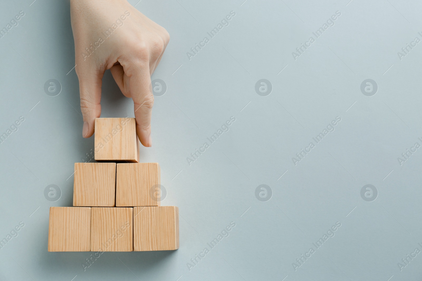 Photo of Woman arranging blank wooden cubes on light background, top view. Space for text