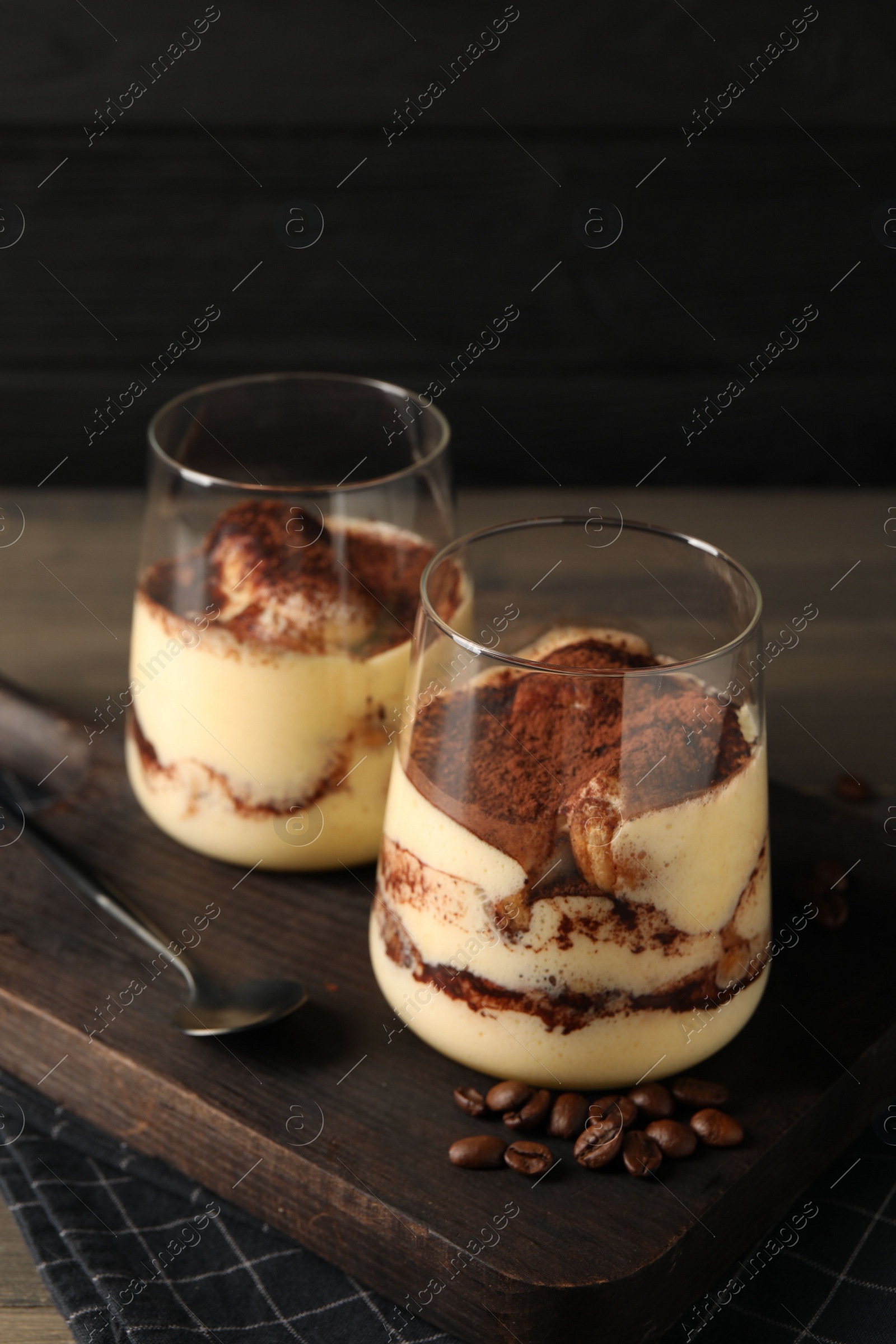 Photo of Delicious tiramisu in glasses, spoon and coffee beans on wooden table, closeup