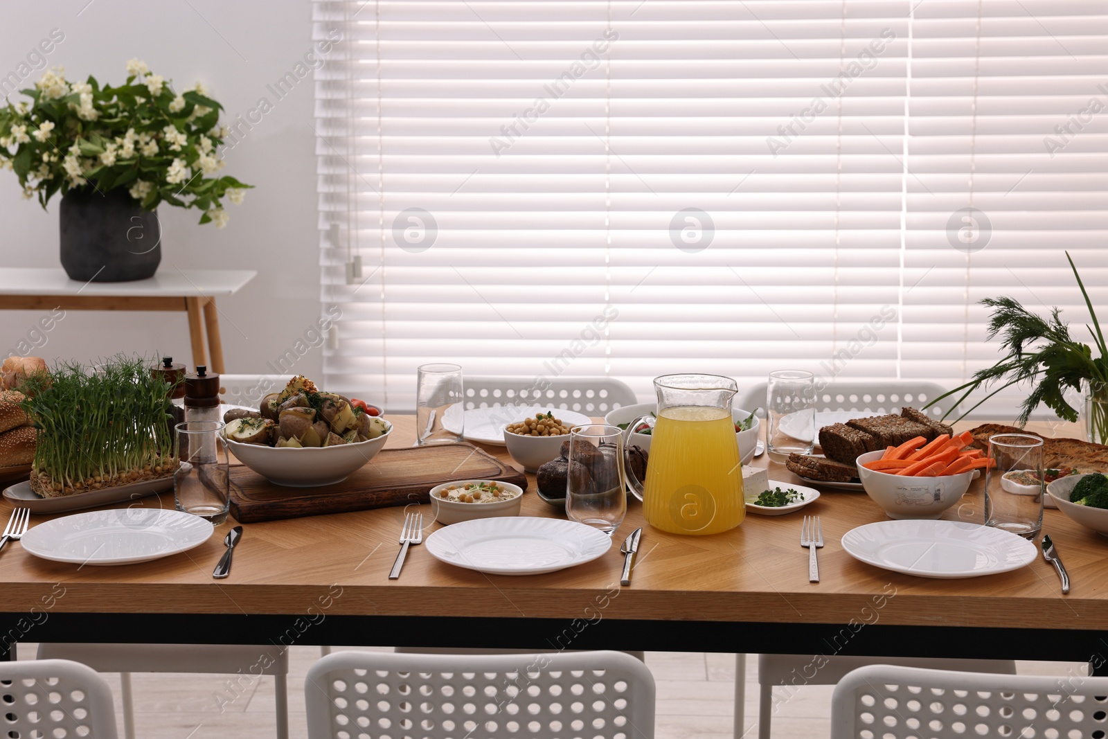 Photo of Healthy vegetarian food, jug of juice, cutlery, glasses and plates on wooden table indoors