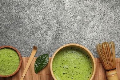 Cup of fresh matcha tea, bamboo whisk, spoon and green powder on grey table, flat lay. Space for text