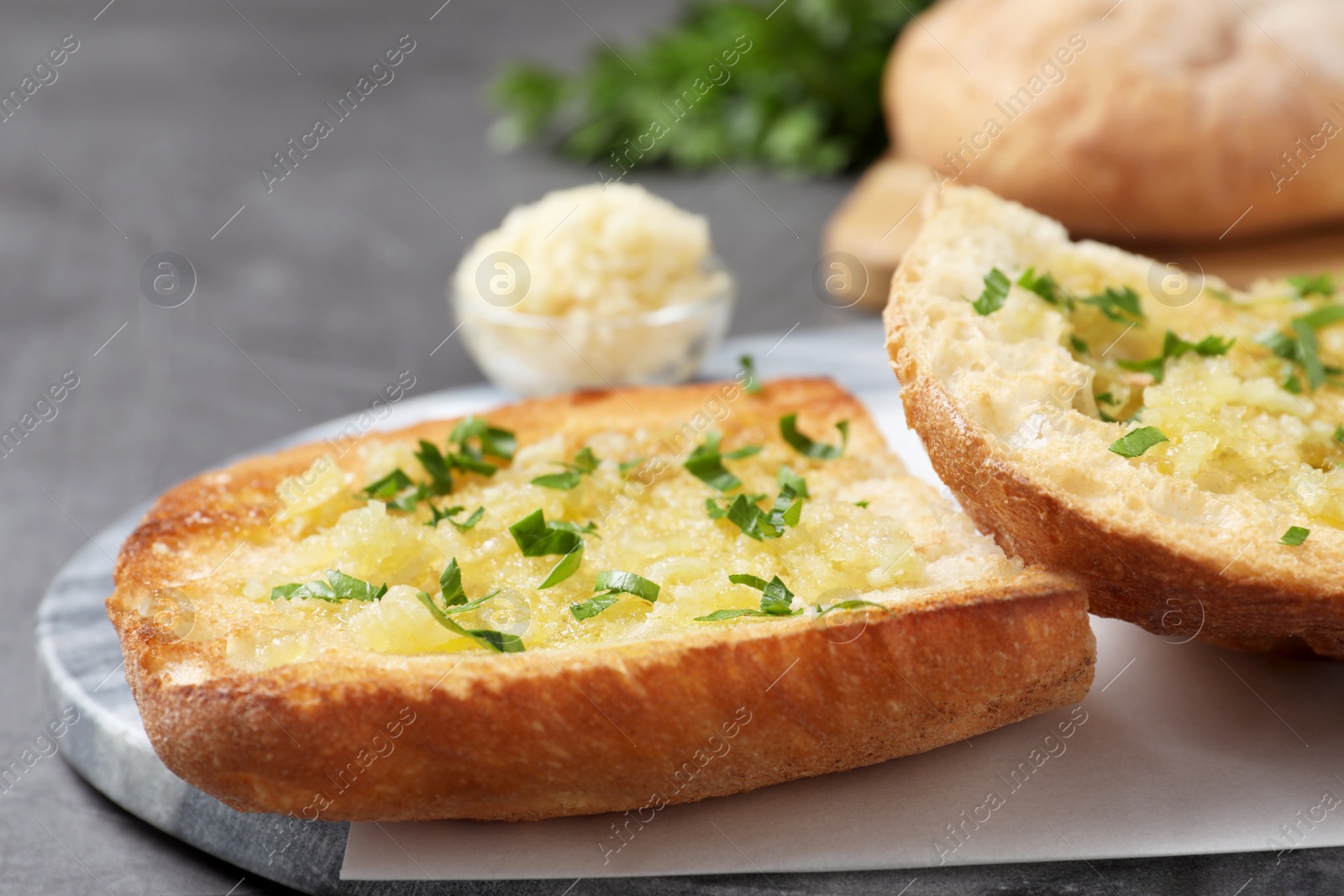 Photo of Slices of delicious toasted bread with garlic and herbs on grey table, closeup