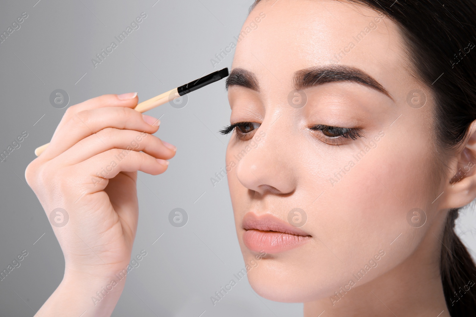 Photo of Beautiful woman with perfect eyebrows applying makeup on light background