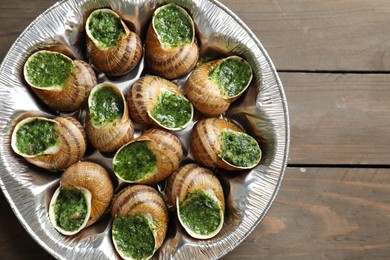 Delicious cooked snails on wooden table, top view. Space for text
