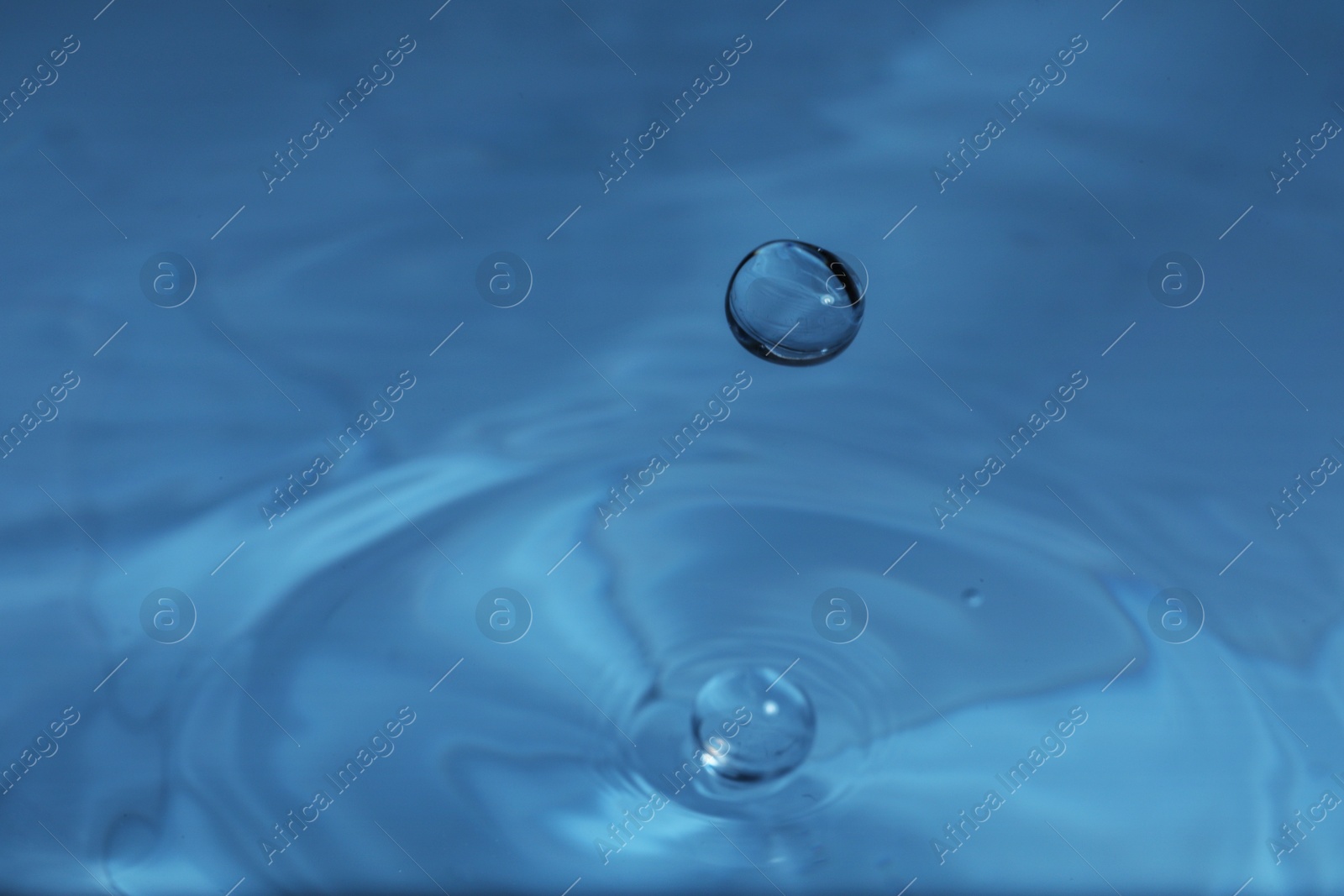 Photo of Drop falling into water on blue background, macro view. Space for text