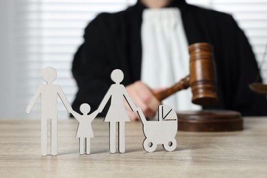 Photo of Family law. Judge with gavel sitting at wooden table, focus on figure of parents and children