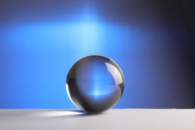 Photo of Transparent glass ball on table against blue background