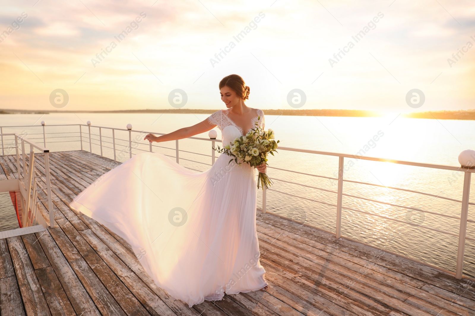 Photo of Gorgeous bride in beautiful wedding dress with bouquet near river on sunset