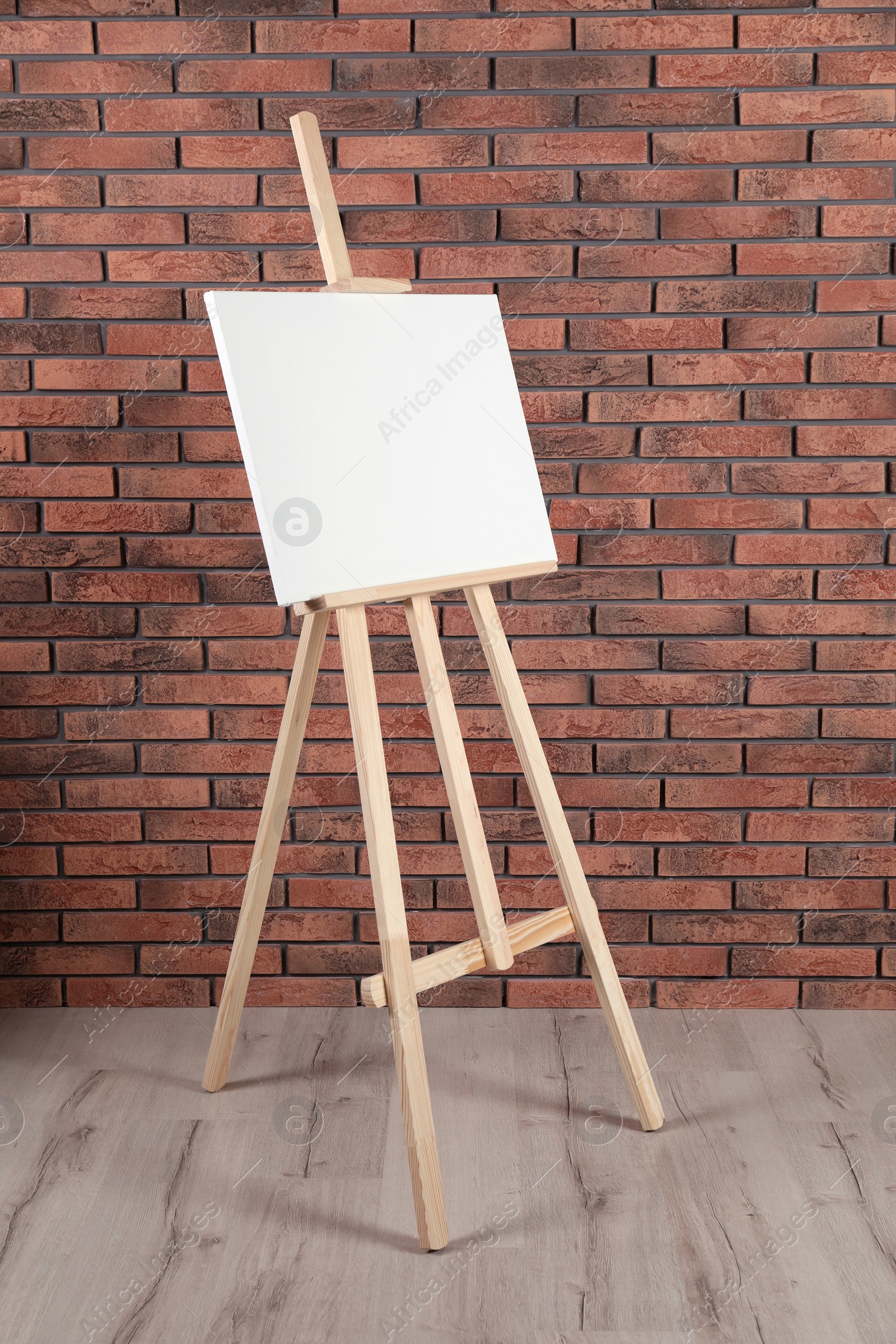 Photo of Wooden easel with blank canvas near brick wall