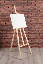 Wooden easel with blank canvas near brick wall