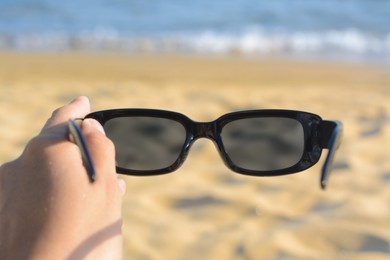 Photo of Woman holding stylish sunglasses near beautiful sea, closeup