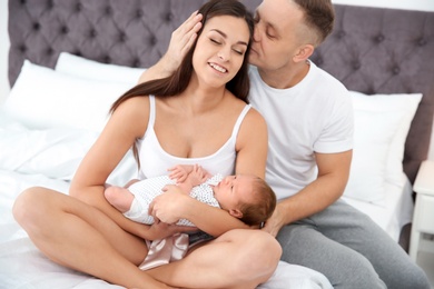 Photo of Happy couple with their newborn baby on bed