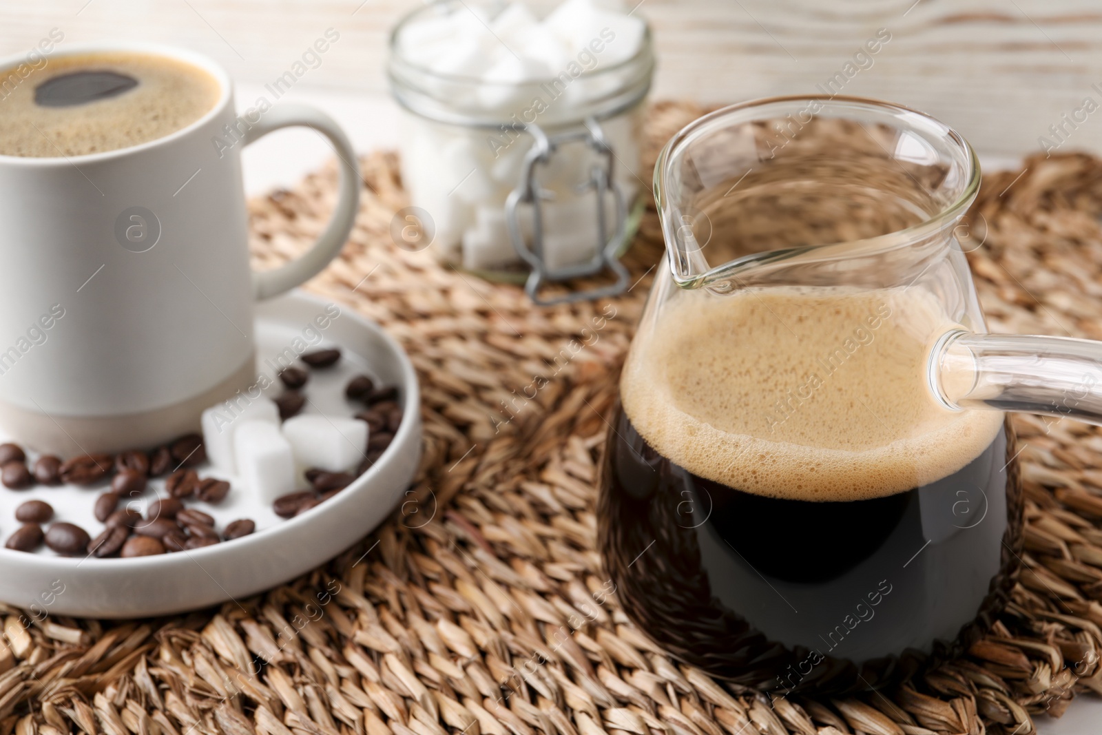 Photo of Turkish coffee. Glass cezve and cup with hot aromatic coffee and sugar on wicker mat