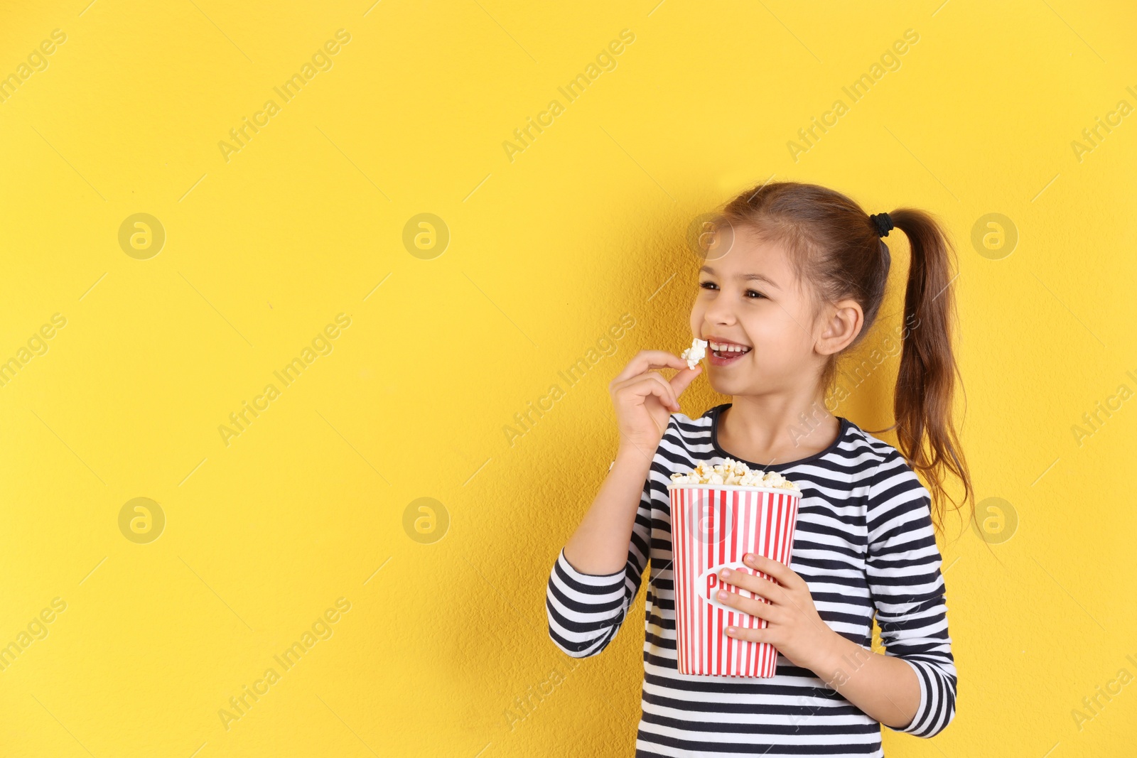 Photo of Cute little girl with popcorn on color background. Space for text