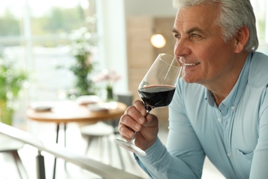 Senior man with glass of wine in restaurant. Space for text