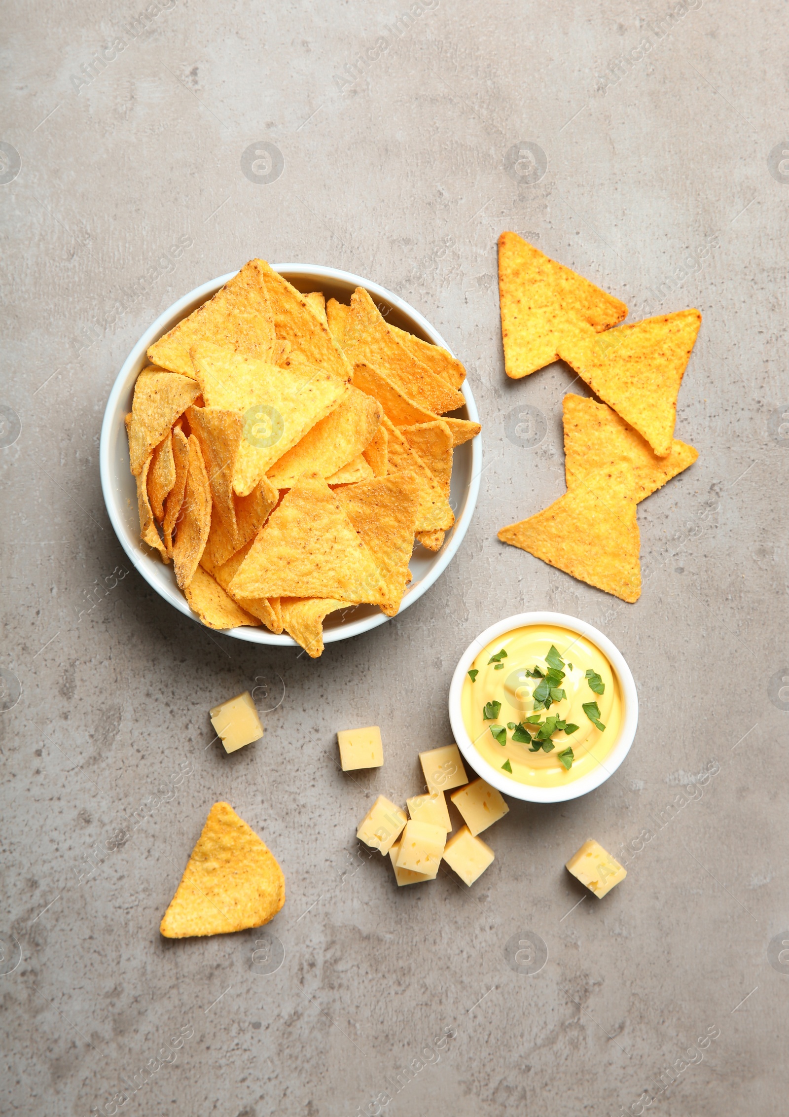 Photo of Bowl of delicious mexican nachos chips and cheese sauce on grey table, flat lay