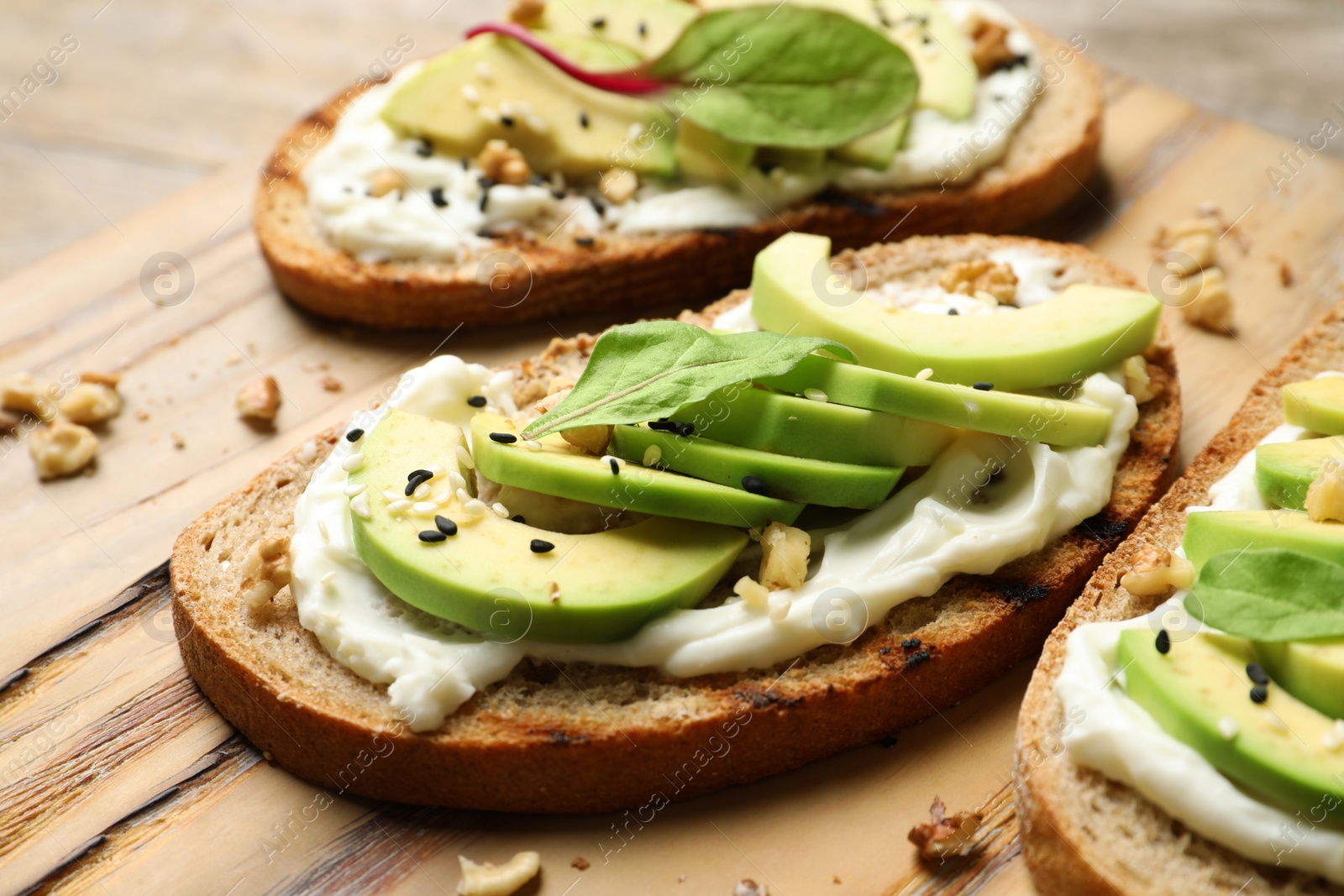 Photo of Delicious bruschettas with avocado served on wooden board, closeup