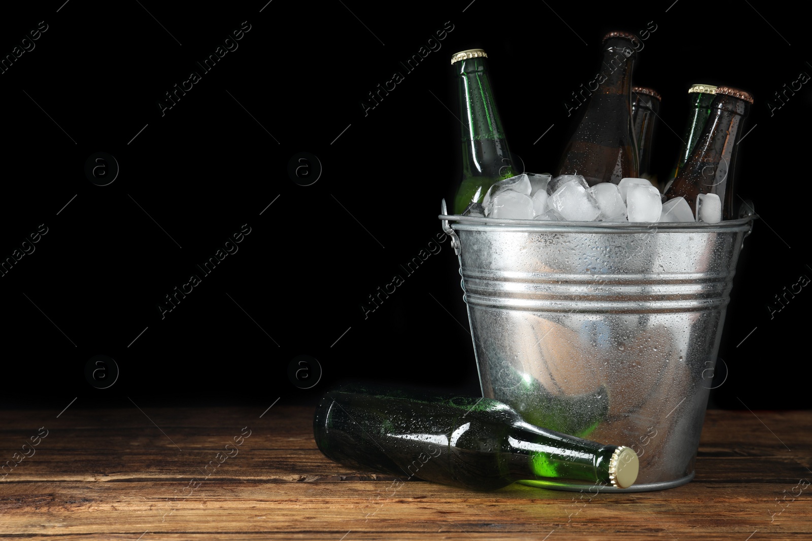 Photo of Metal bucket with bottles of beer and ice cubes on wooden table. Space for text