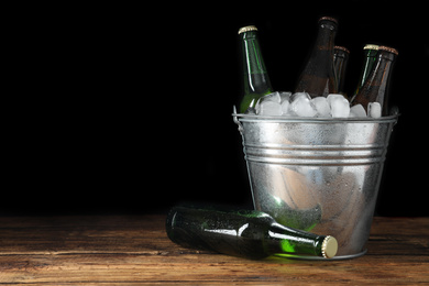 Metal bucket with bottles of beer and ice cubes on wooden table. Space for text