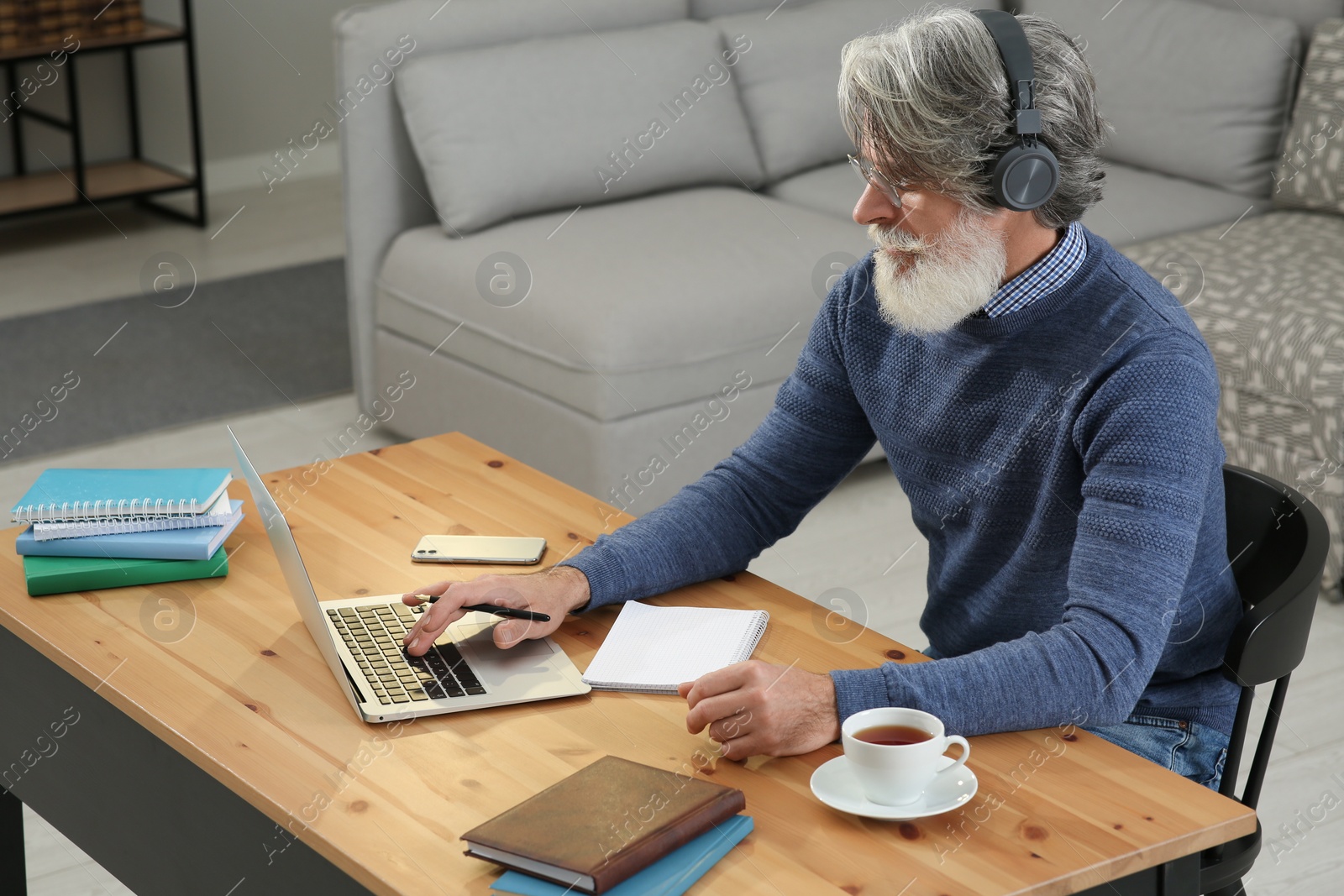 Photo of Middle aged man with laptop and headphones learning at table indoors