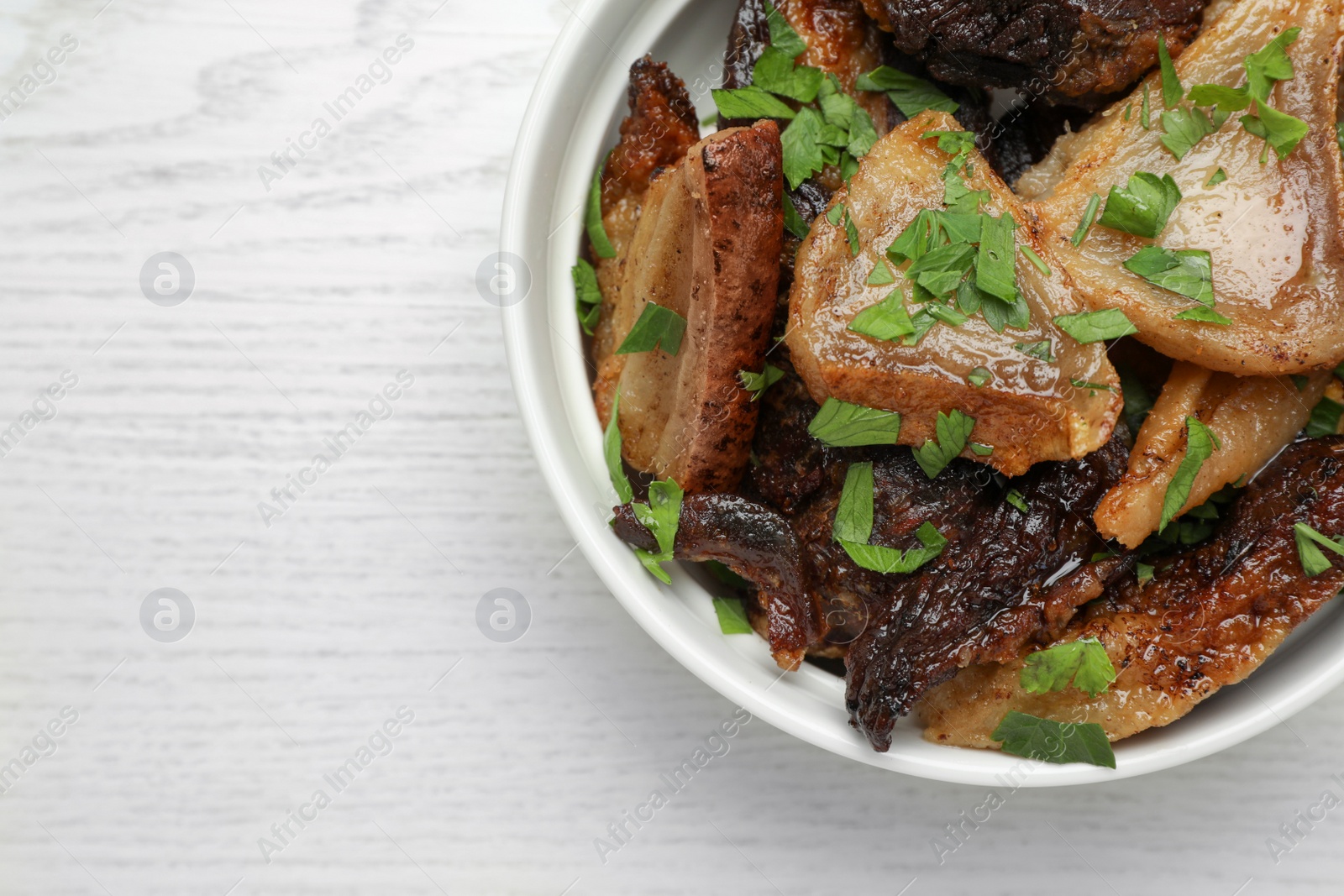 Photo of Tasty fried cracklings with parsley on white wooden table, top view and space for text. Cooked pork lard