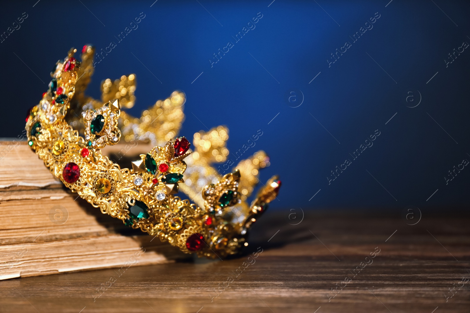 Photo of Beautiful golden crown and old books on wooden table, space for text. Fantasy item