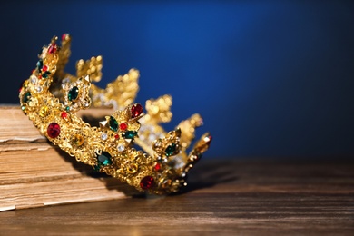 Photo of Beautiful golden crown and old books on wooden table, space for text. Fantasy item