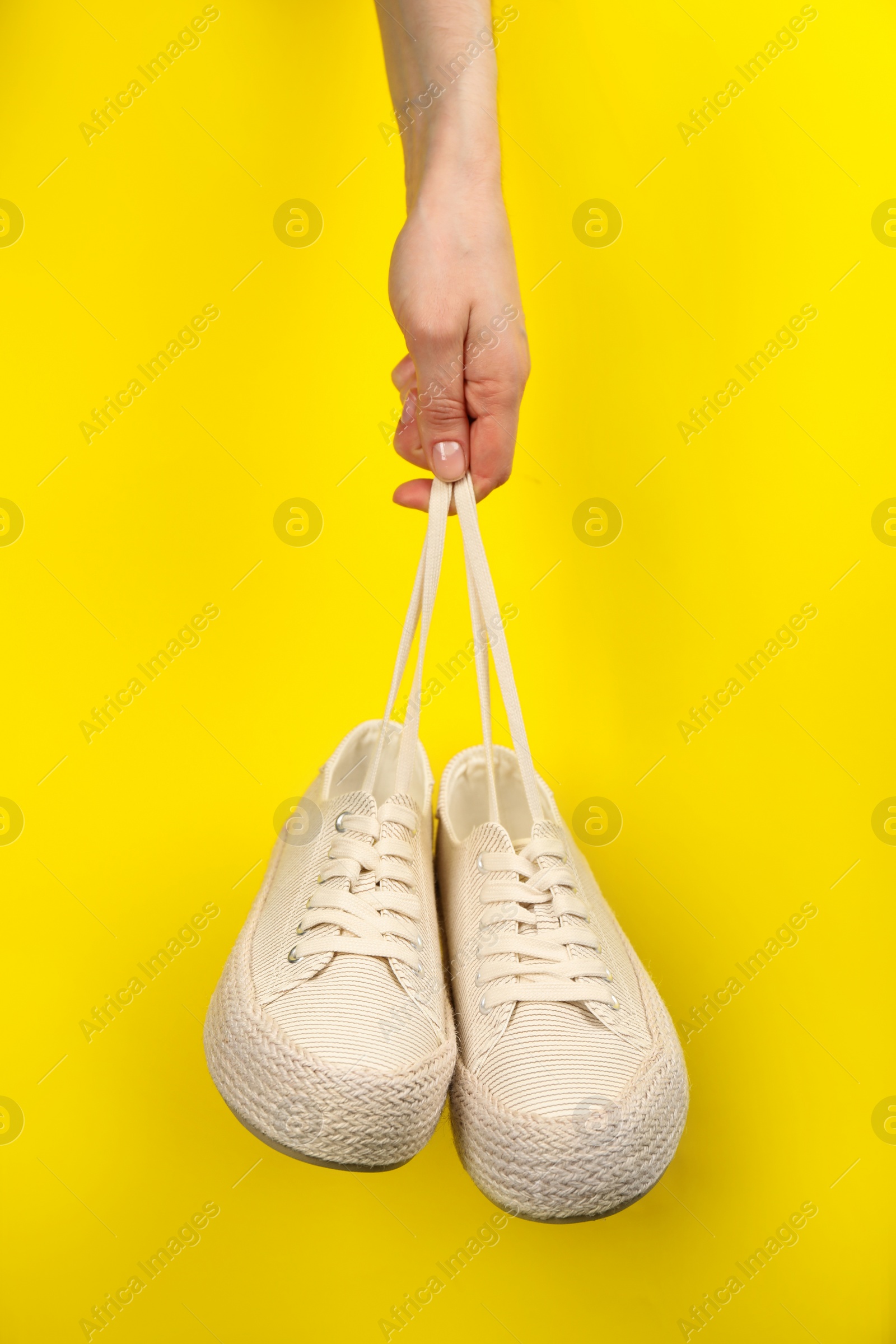 Photo of Woman holding pair of stylish comfortable shoes on yellow background, closeup