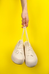 Photo of Woman holding pair of stylish comfortable shoes on yellow background, closeup