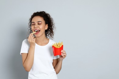 African American woman with French fries on grey background, space for text